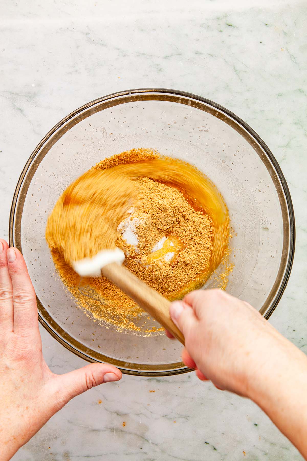 A hand mixing graham crust ingredients with a rubber spatula.