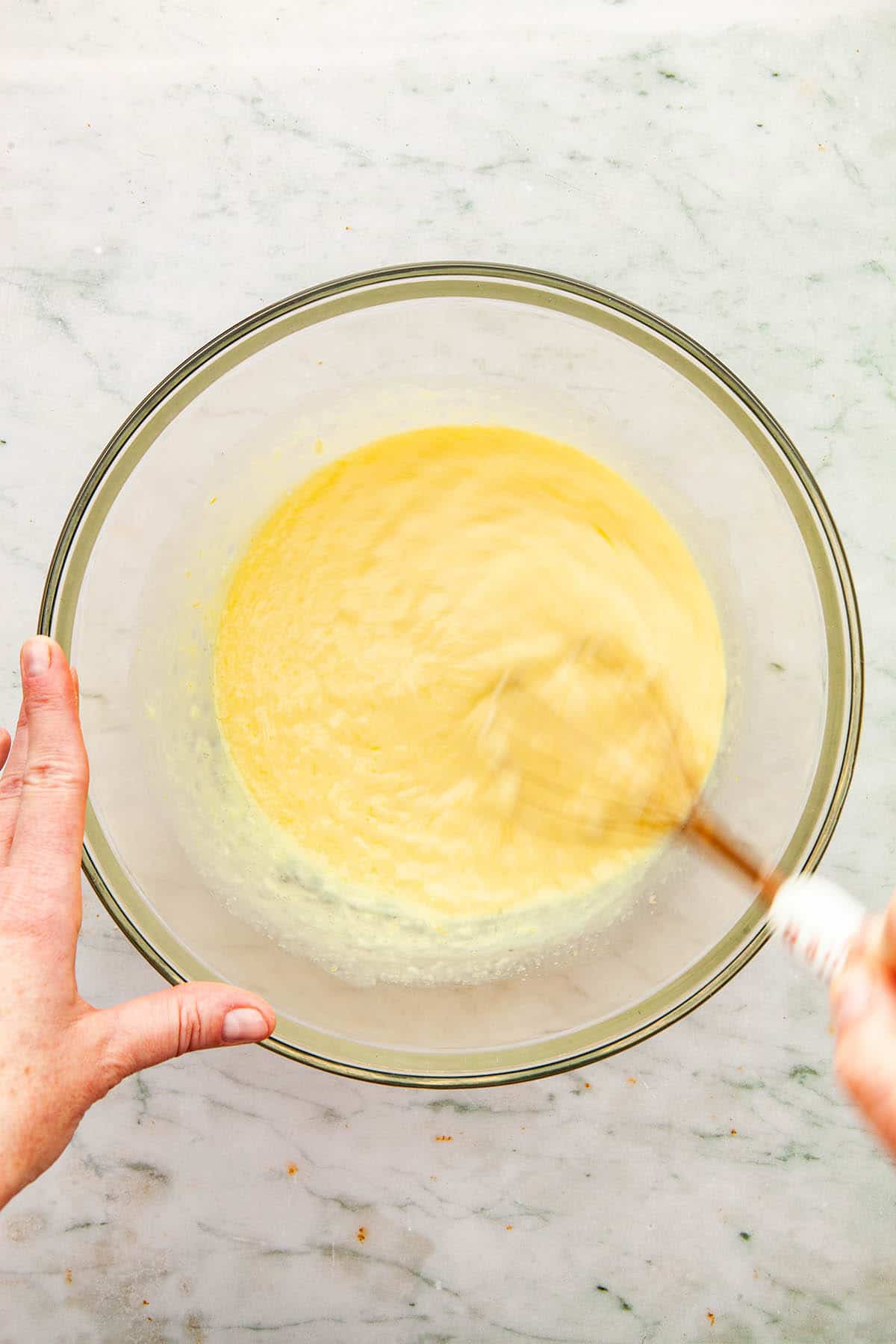A hand whisking lemon filling in a large glass bowl.