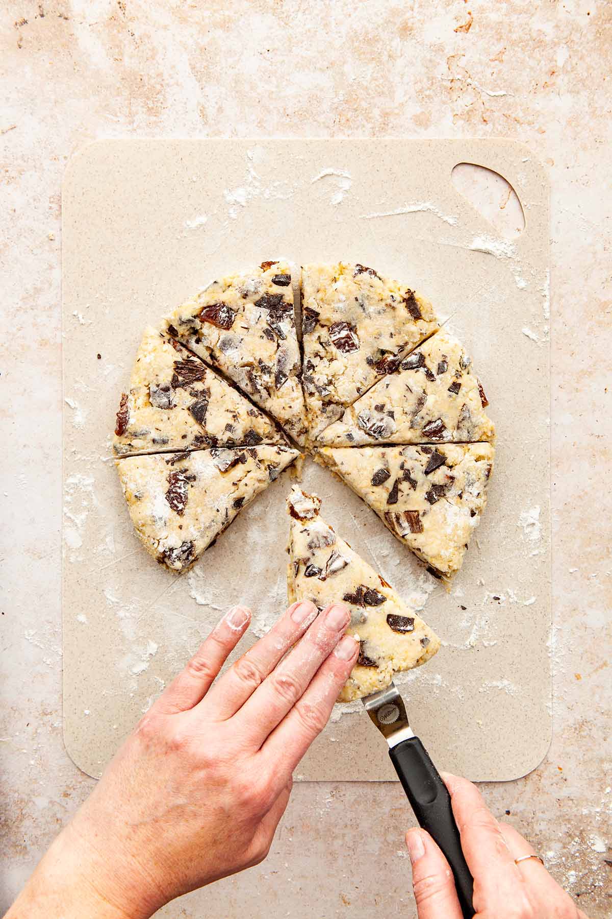 Hands lifting a scone from a work surface with a small offset spatula.