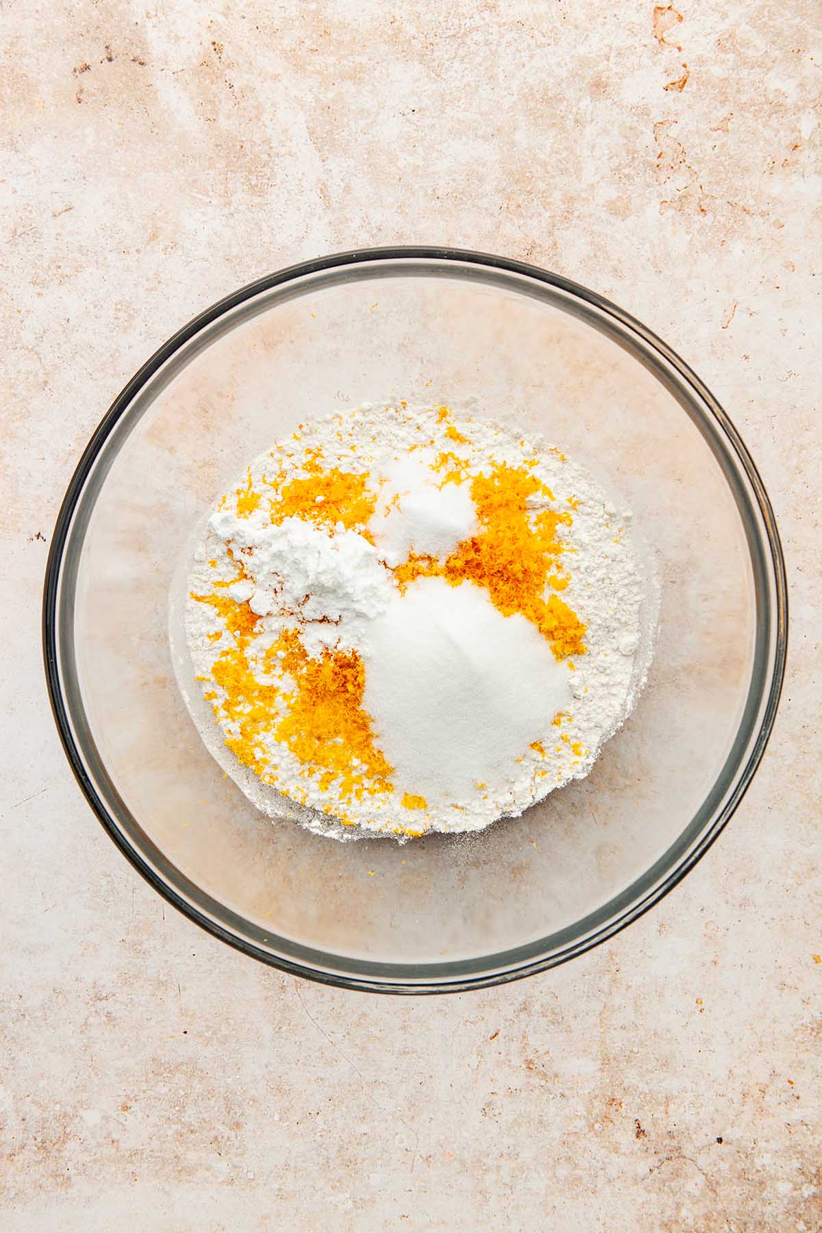 A bowl of flour with sugar, orange zest, baking powder, and salt.