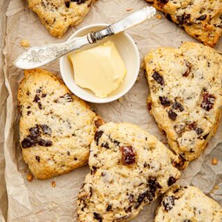 Date and orange scones piled ina. box lined with parchment paper with a small dish of butter and a tiny pearl-handled knife.