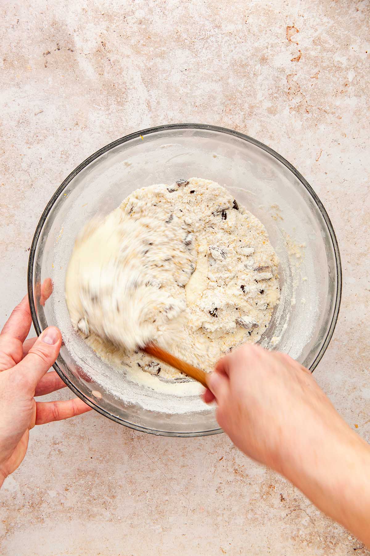 A hand mixing dry and wet dough ingredients with a wooden spoon.
