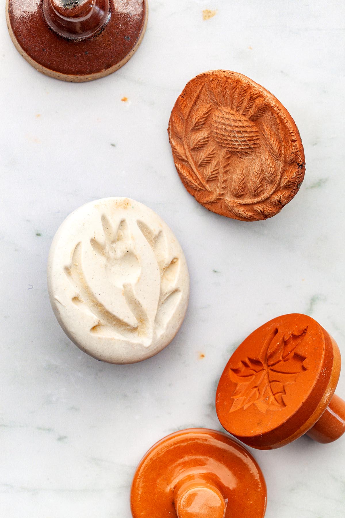 Two thistle shortbread stamps and other ceramic cookie stamps laying down on a marble surface.