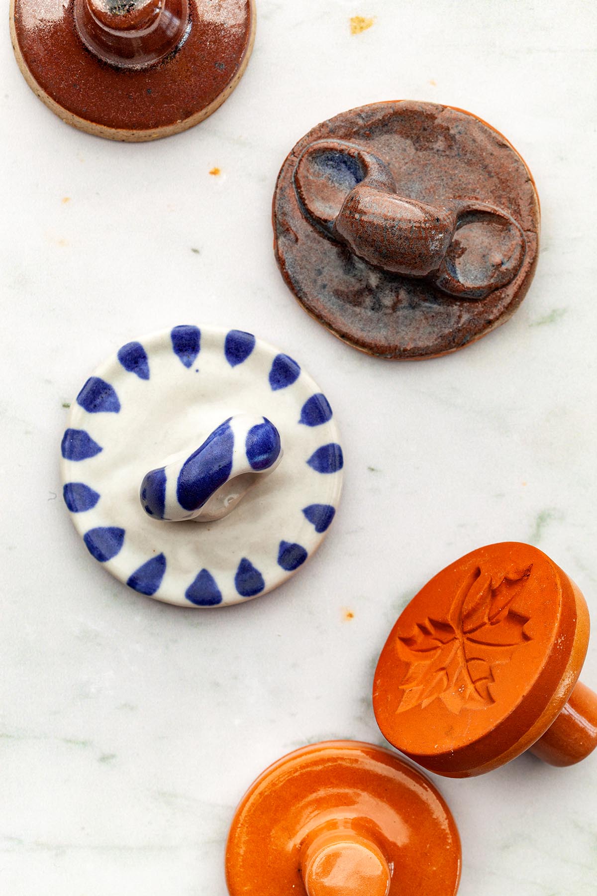 A thistle shortbread stamp and other ceramic cookie stamps laying down on a marble surface.