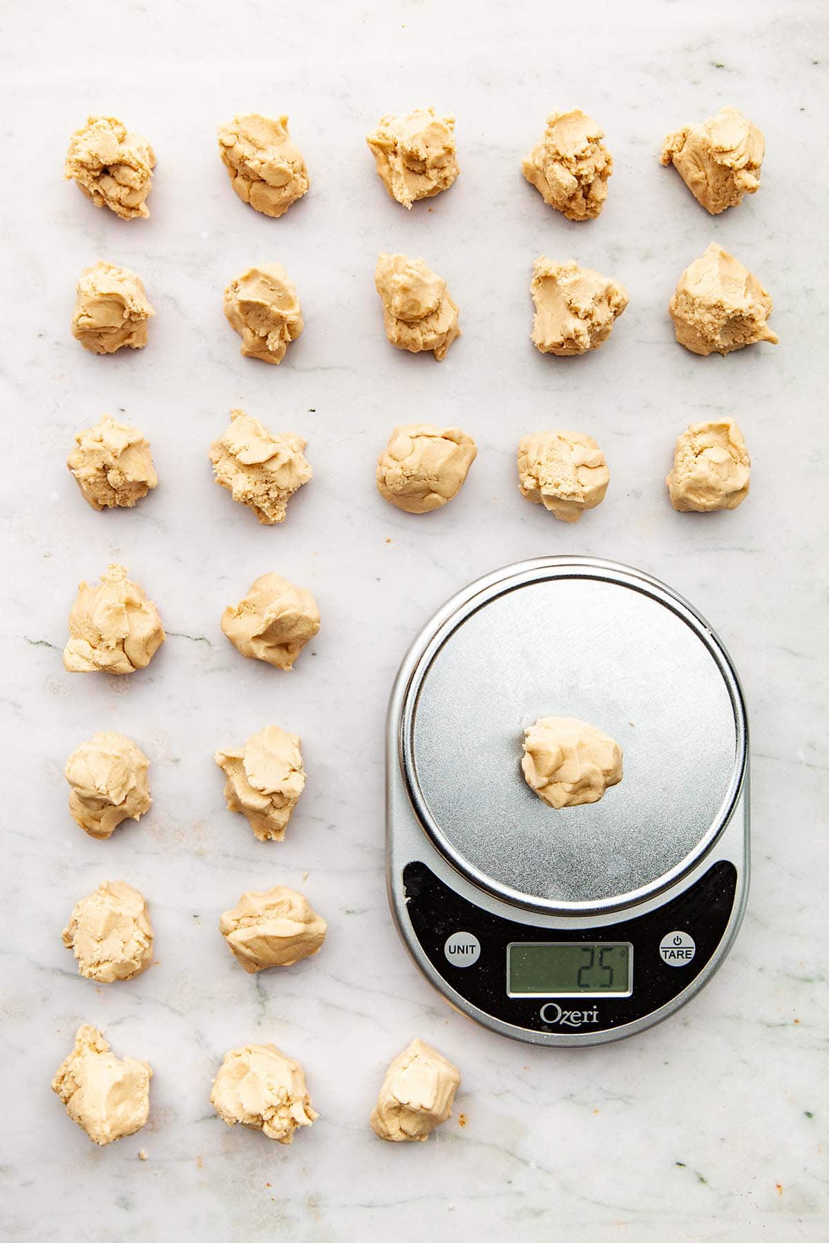 Two dozen portions of dough at 25 grams per piece with one portion on a silver digital scale.