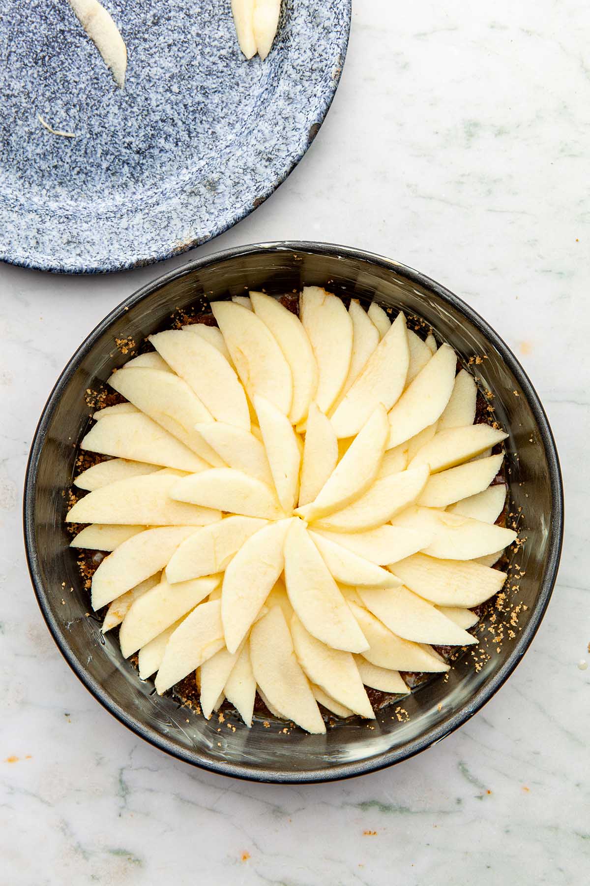 Apple slices arranged in a circular pattern inside a cake tin.