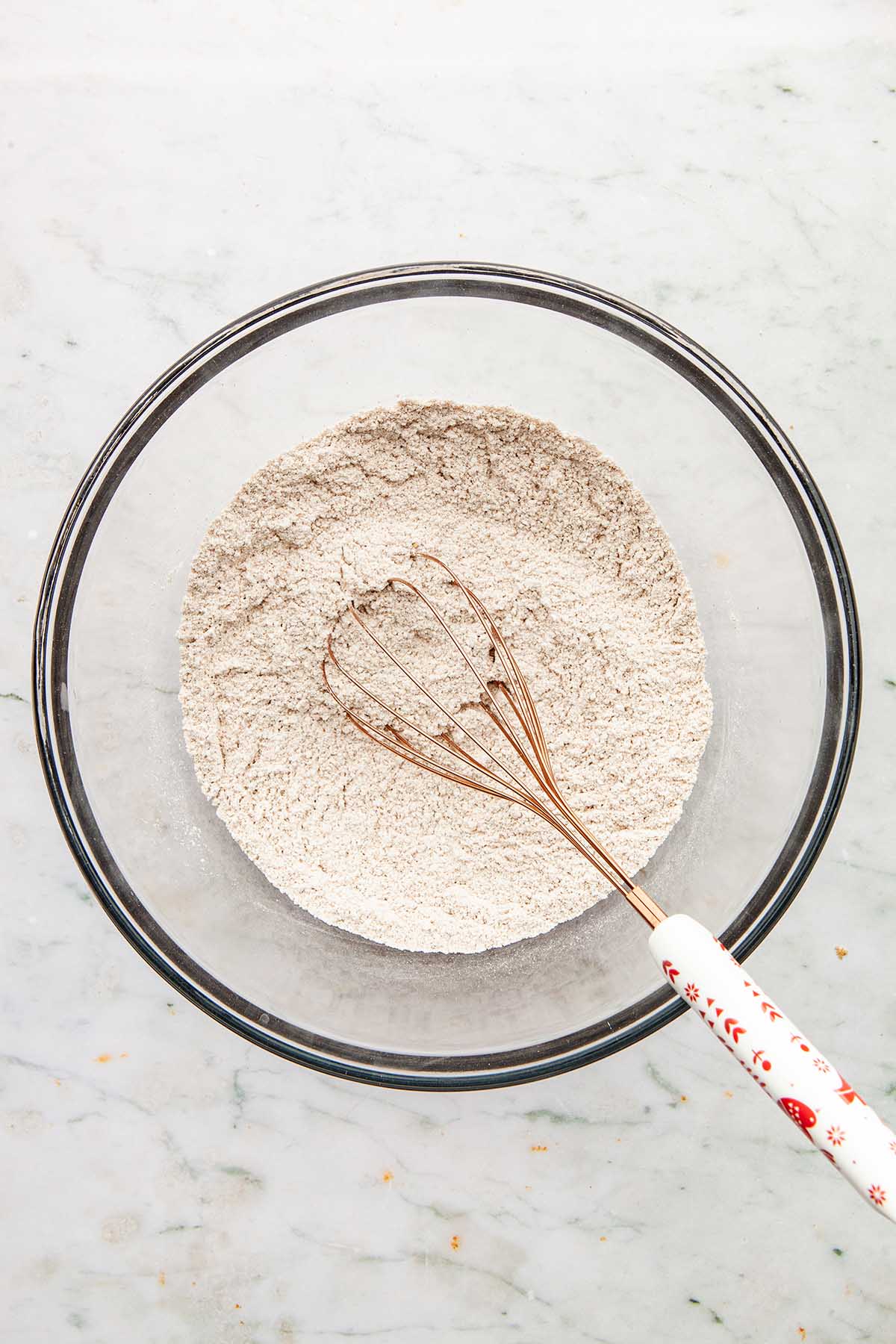 A bowl of whisked dry ingredients with the whisk in the glass bowl.