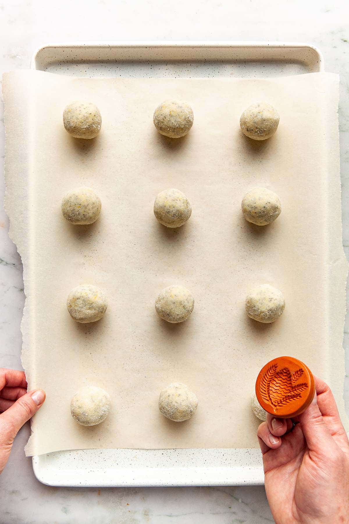 A hand about to stamp sugar-coated cookie dough balls with a ceramic cookie stamp.