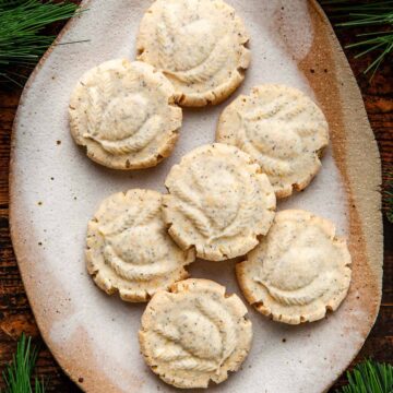 A small oval platter of lemon poppy seed shortbread cookies surrounded by evergreen branches.