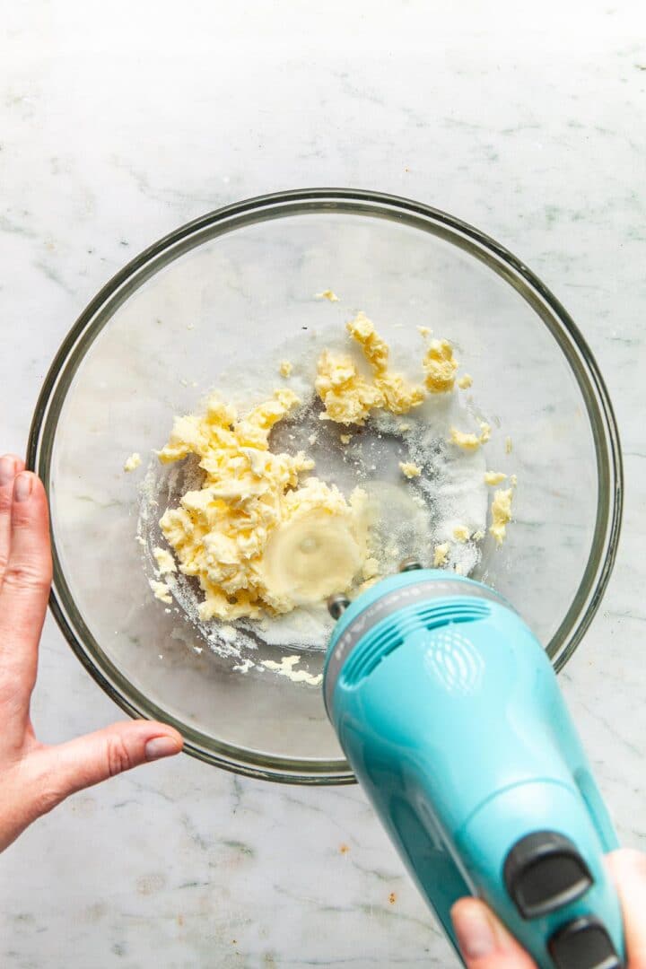 A hand mixer being used to beat together butter and sugar.