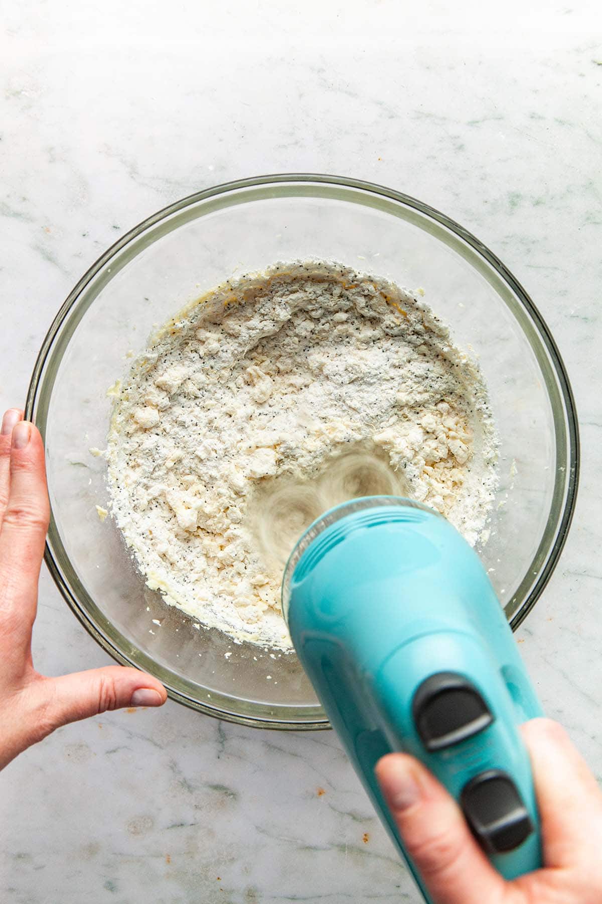 A hand mixer being used to mix flour and butter.