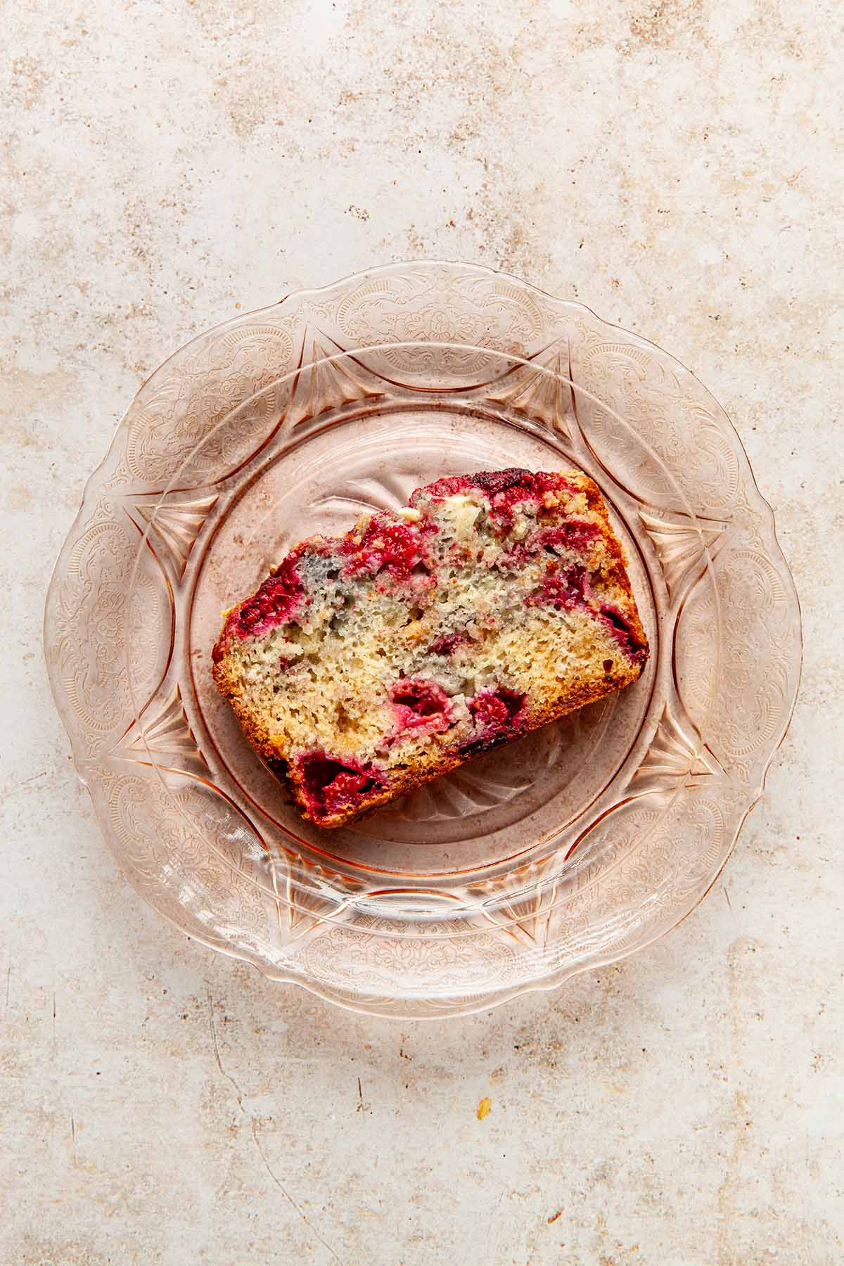 A slice of raspberry and white chocolate loaf cake on a pink Depression glass plate.