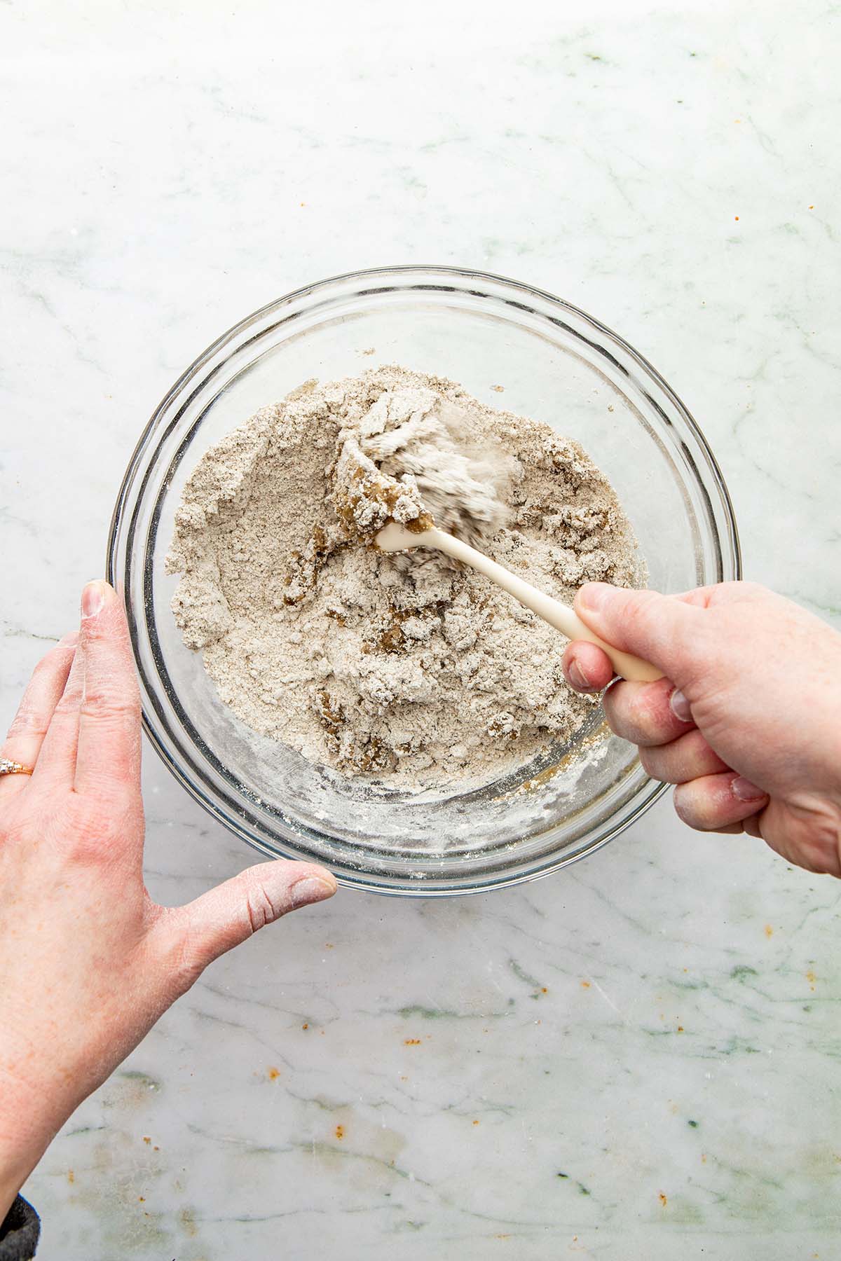 A hand using a for to stir melted butter into a bowl of dry ingredients.