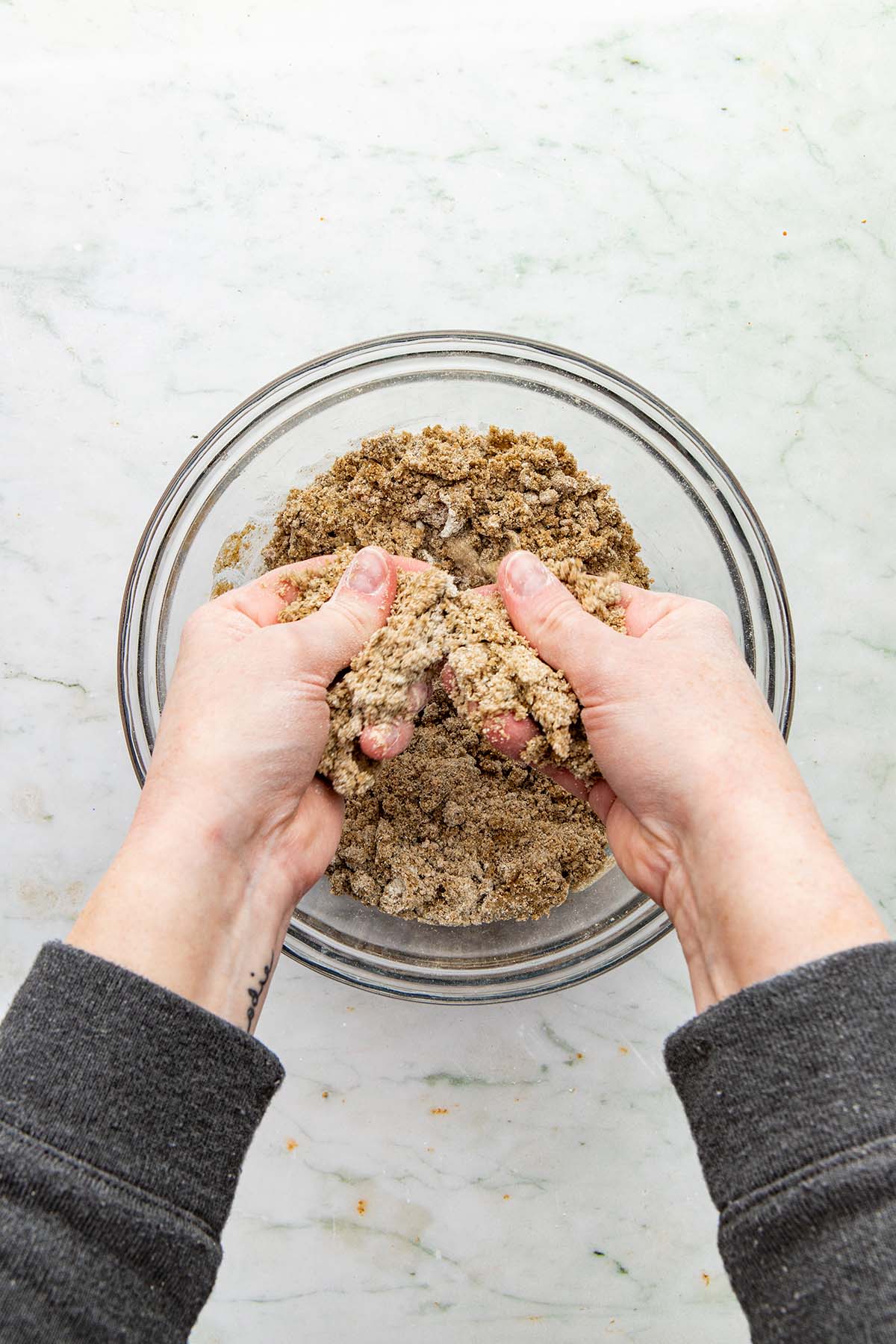 Hands rubbing melted butter into dry crumble topping ingredients.
