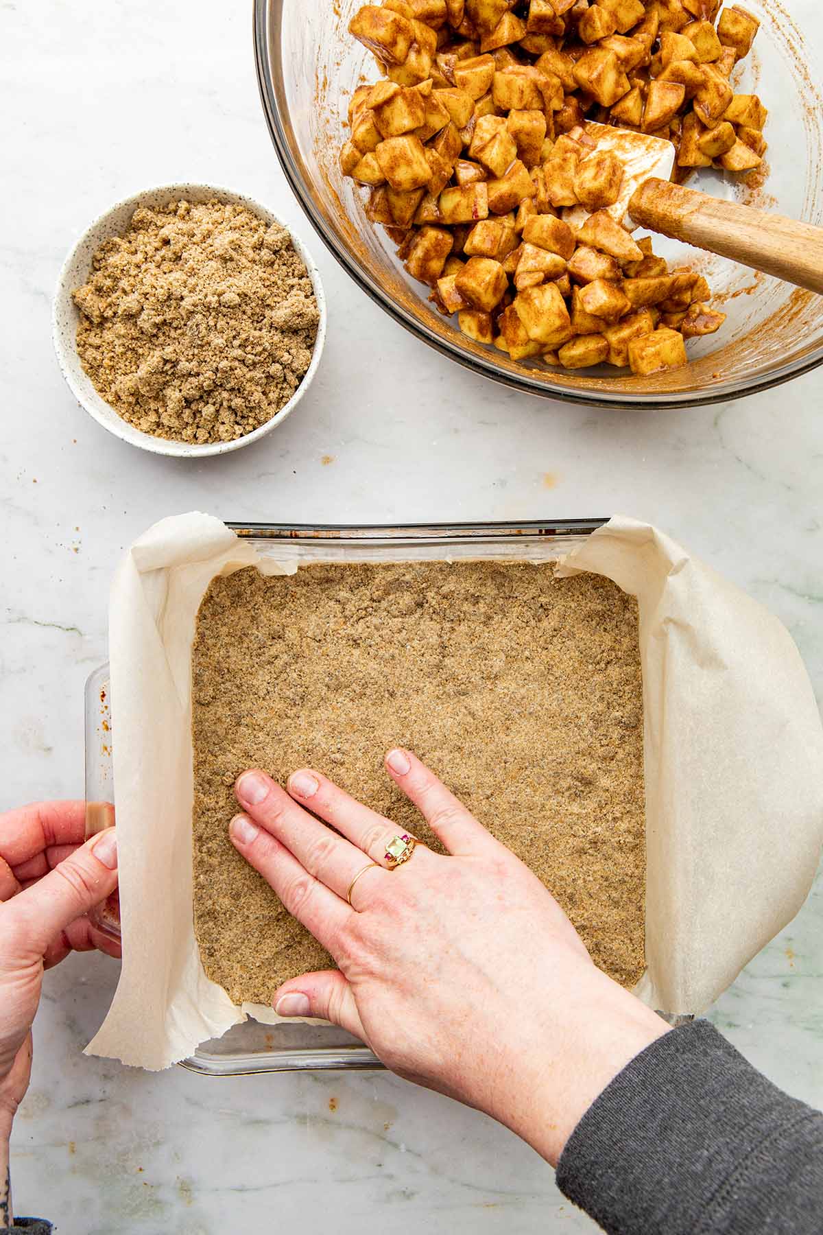 A hand pressing rye flour crust into a square baking dish lined with parchment paper.