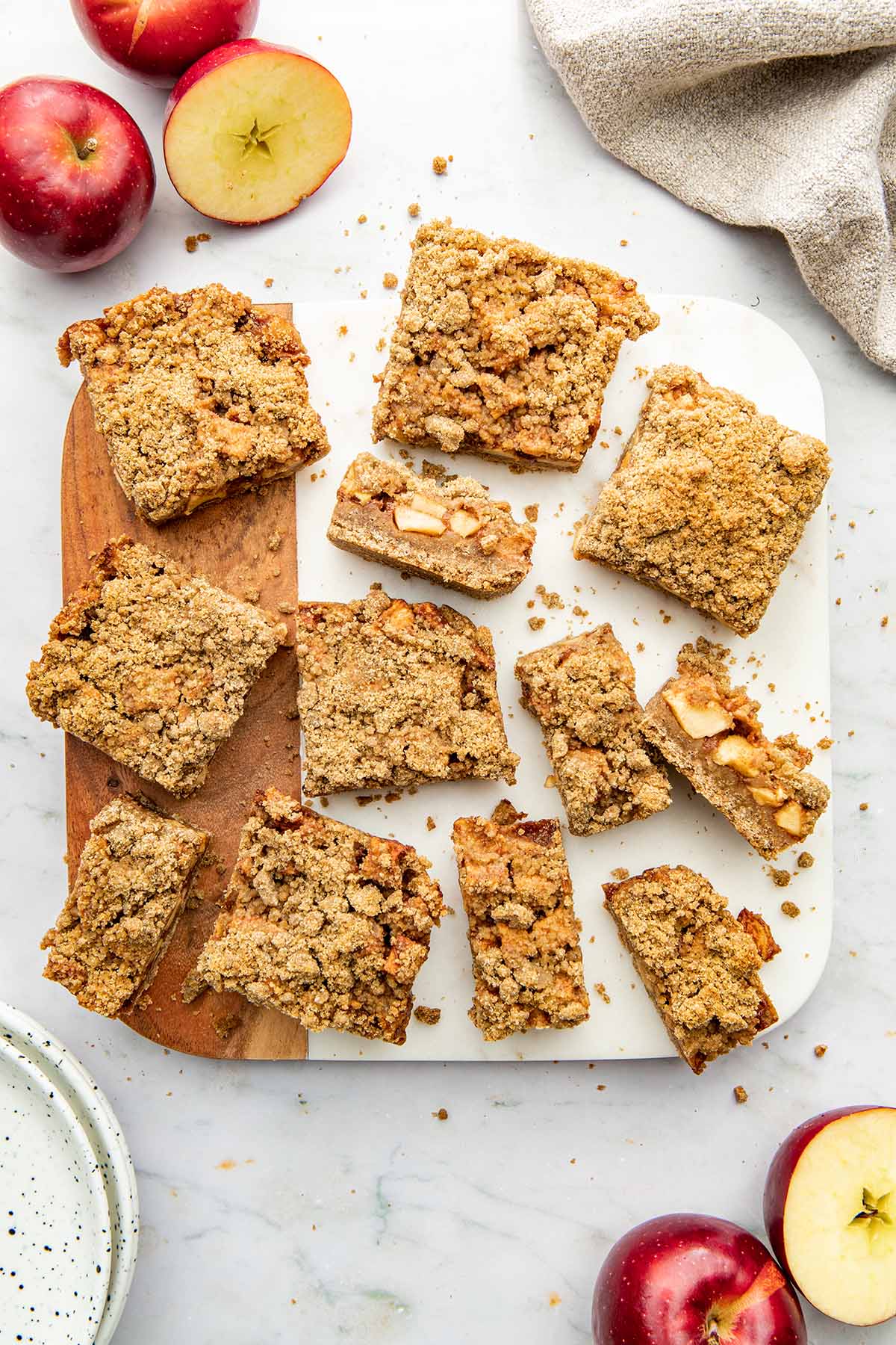 Apple crumble bars sliced into different sizes on a marble and wood square serving board.