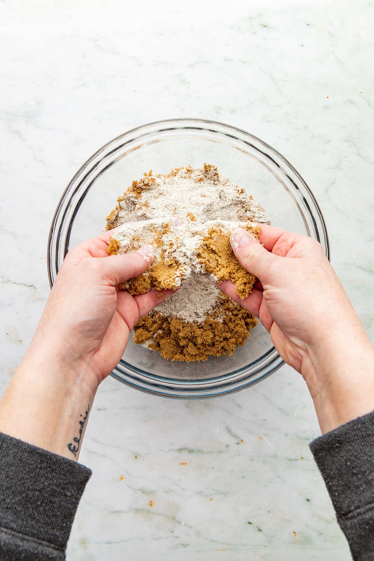 Hands rubbing together dry crumble topping ingredients.