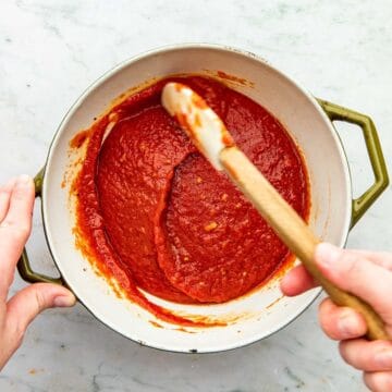 A hand stirring tomato sauce in a pot with a rubber spatula.