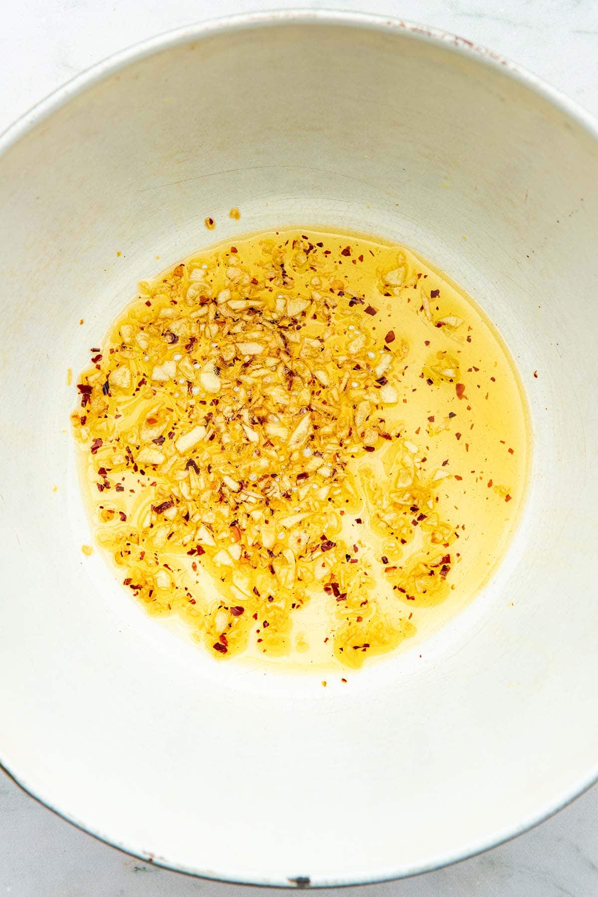 Lightly cooked garlic and chilli flakes in olive oil inside the bottom of a pot.