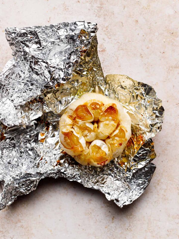 A bulb of air fryer roasted garlic sitting on the piece of aluminum foil it was cooked in.