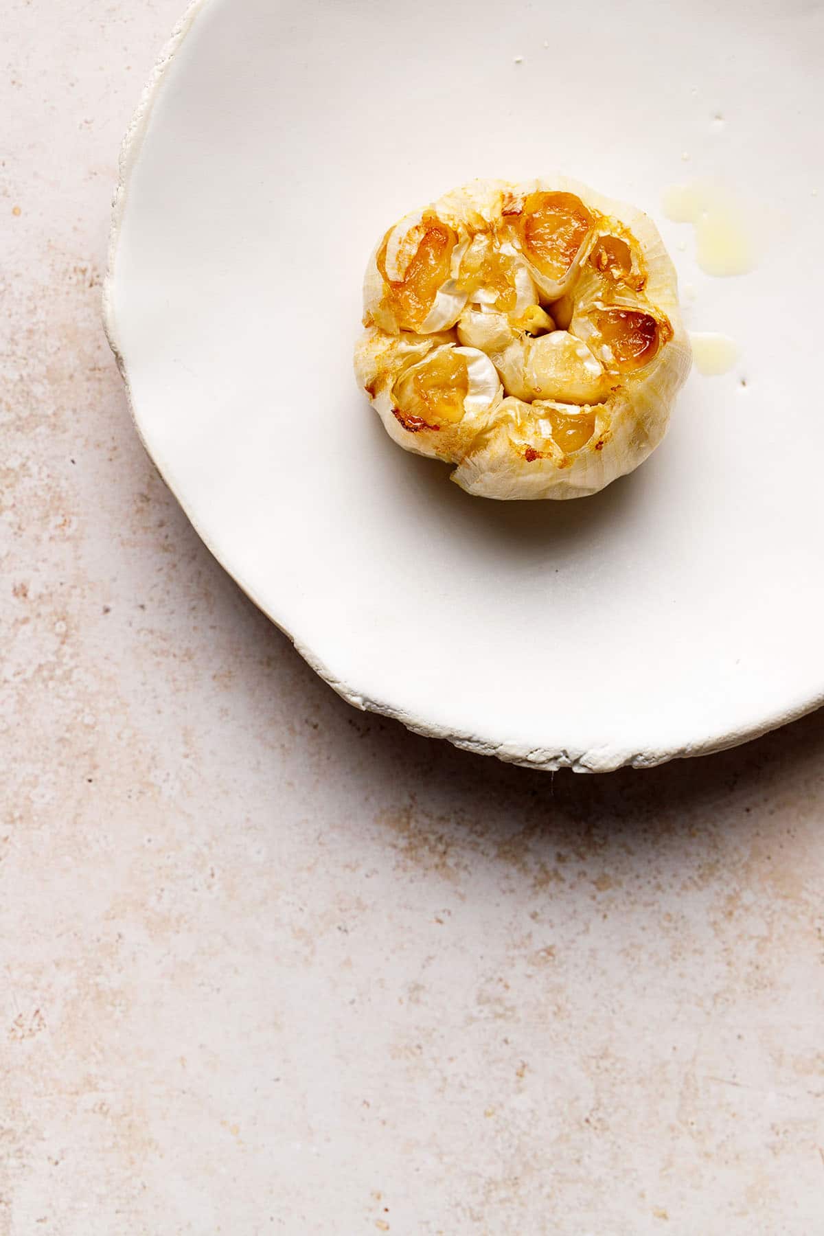 A bulb of air fryer roasted garlic on a white porcelain plate.