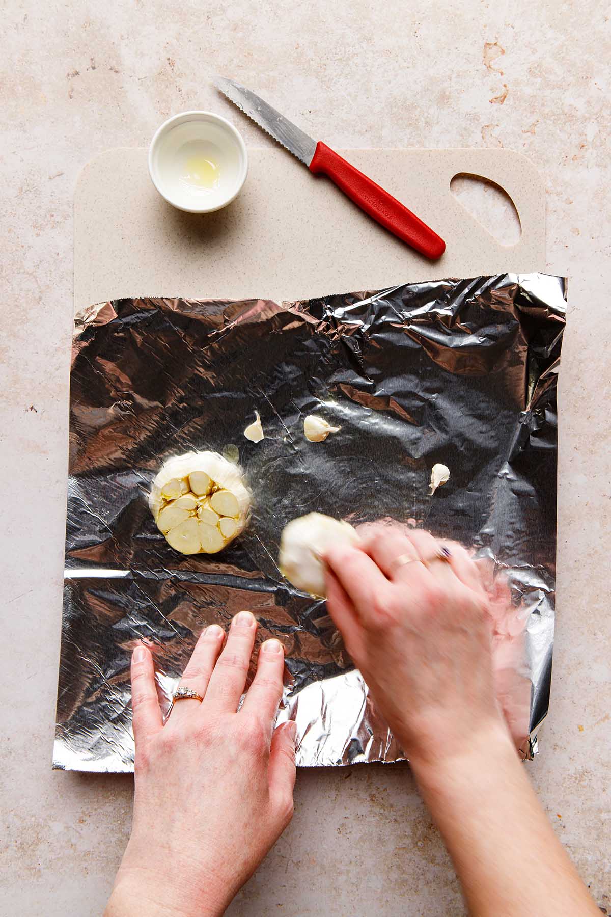 Hands rubbing garlic in oil on a piece of foil.