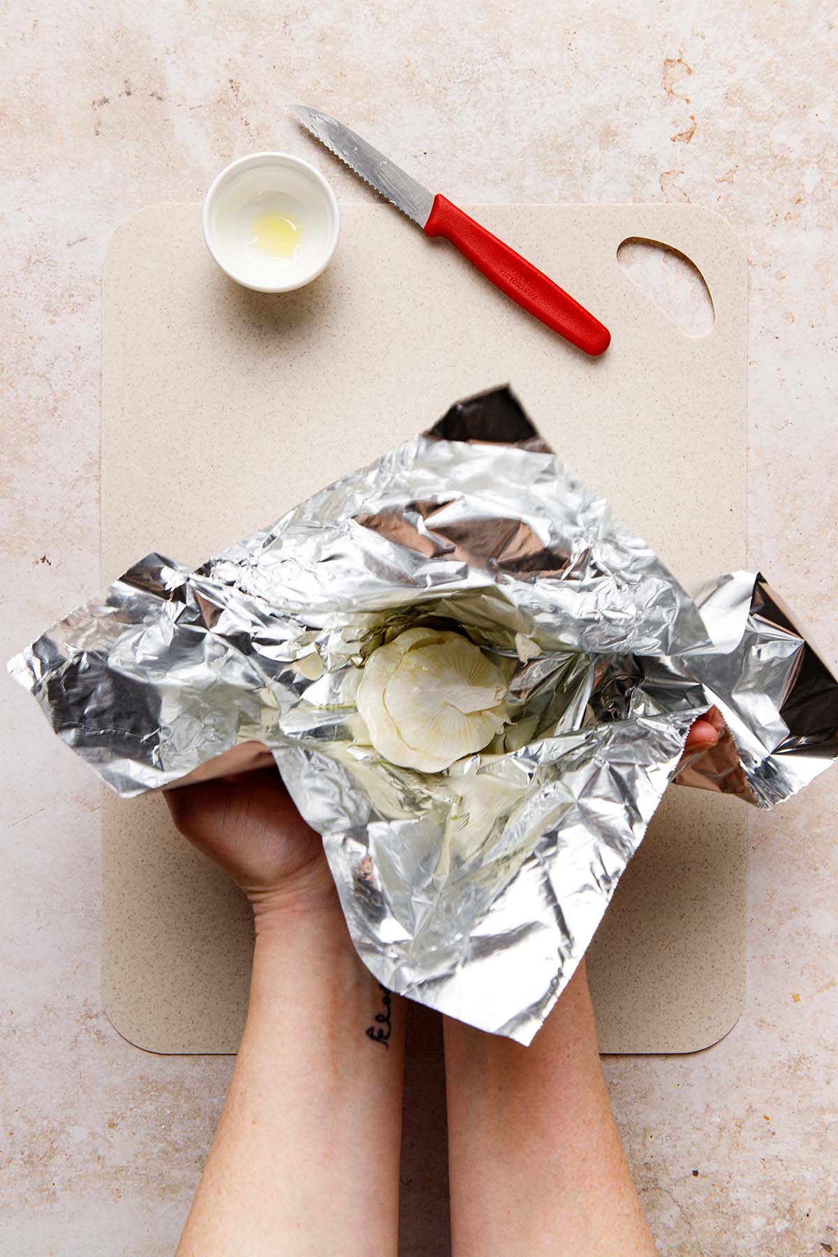 Hands wrapping garlic in foil.