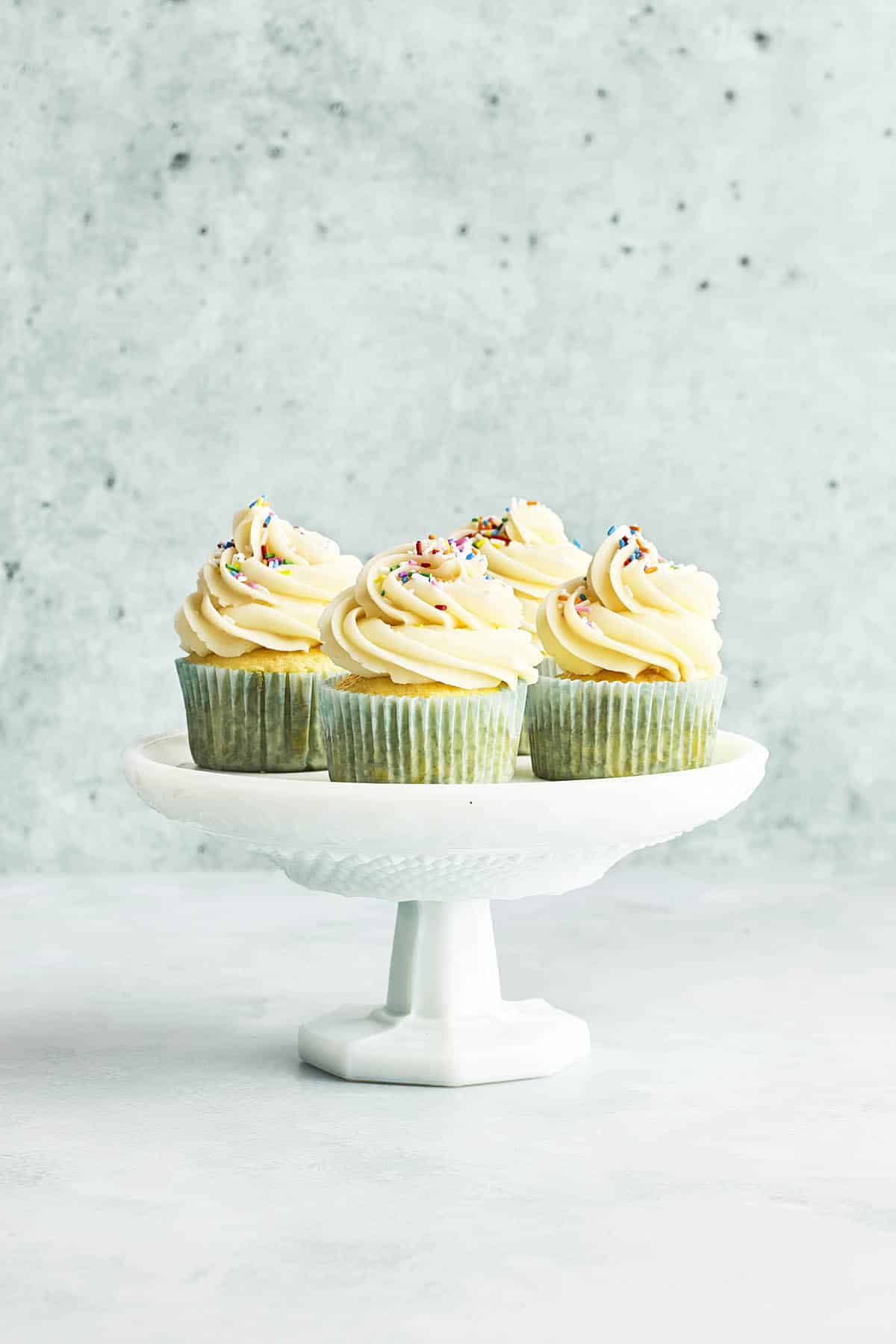 A cake stand with four cupcakes topped with American buttercream resting on top.