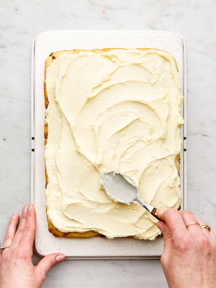 A hand spreading Nanny Burke's buttercream on a sheet cake with the back of a spoon.