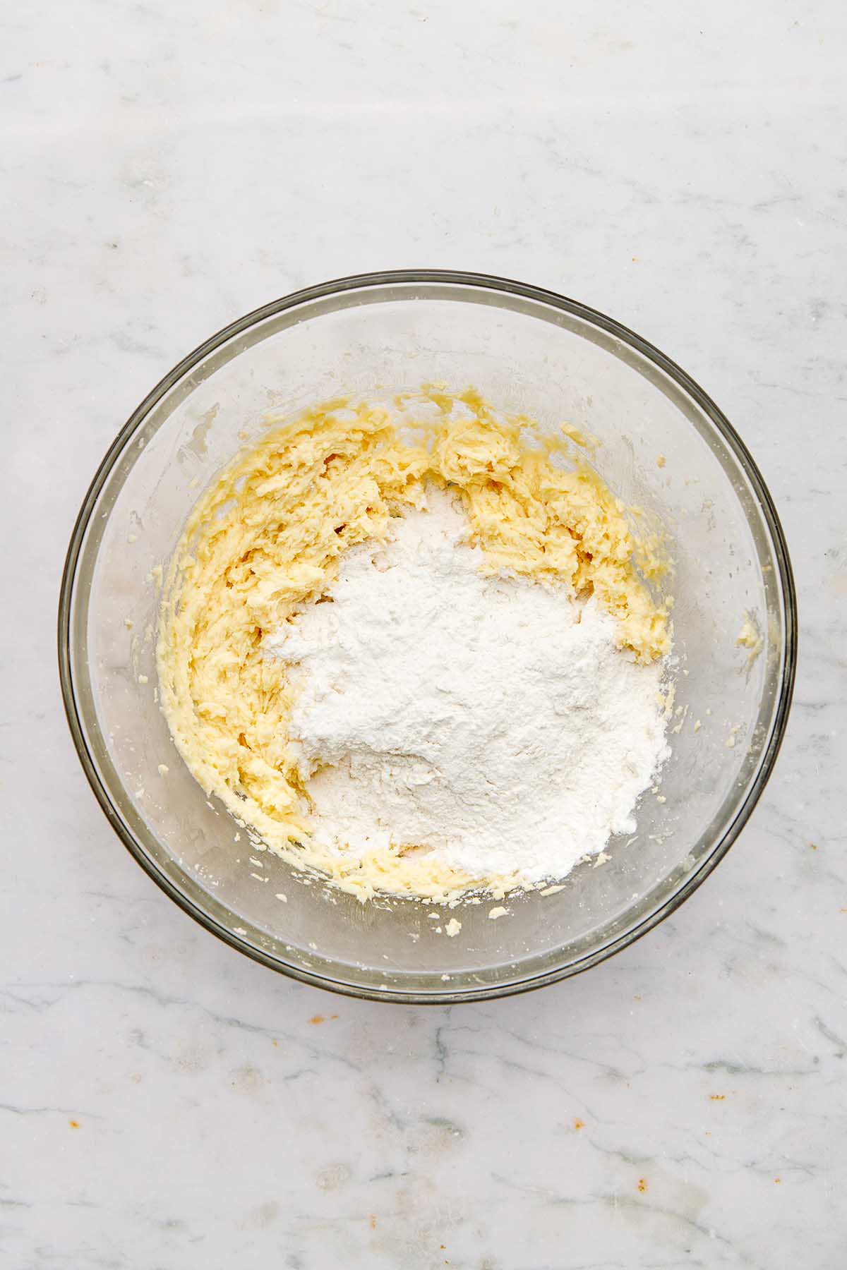 Beaten butter and sugar in a glass bowl with a small pile of flour on top.