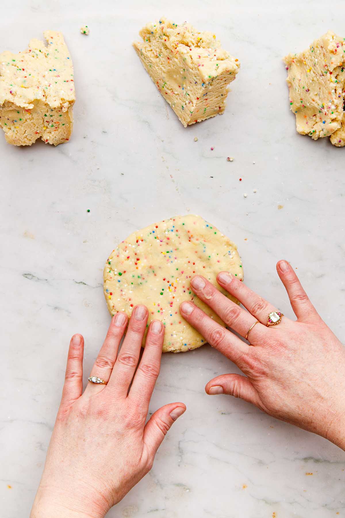 Hands forming a chunk of cookie dough into a flat disc.