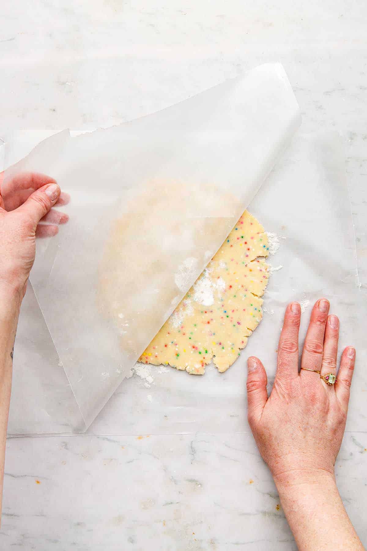A hand peeling wax paper from the top of rolled out cookie dough.