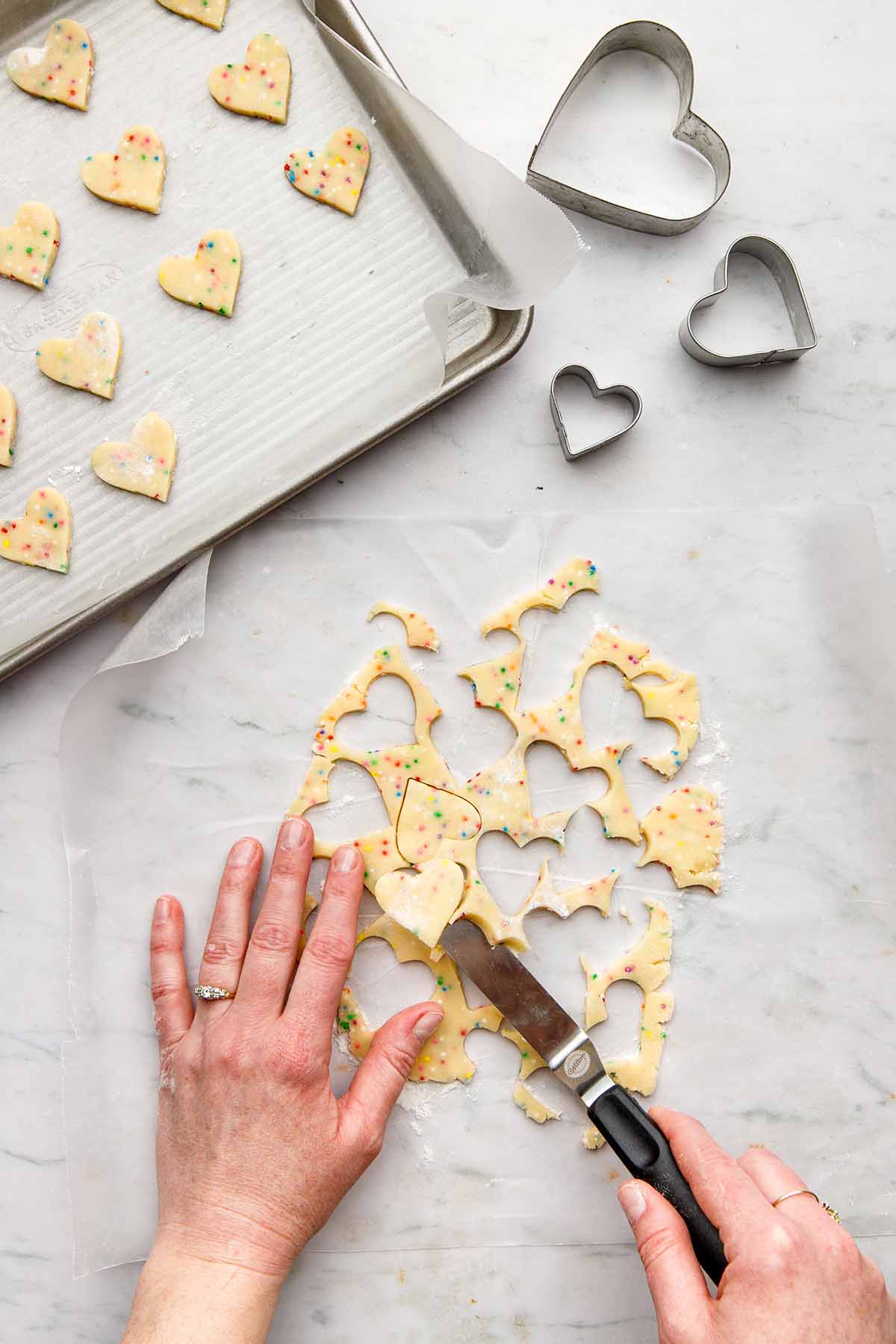 Hands lifting cookie cutouts with an offset spatula to place them on a small baking sheet.
