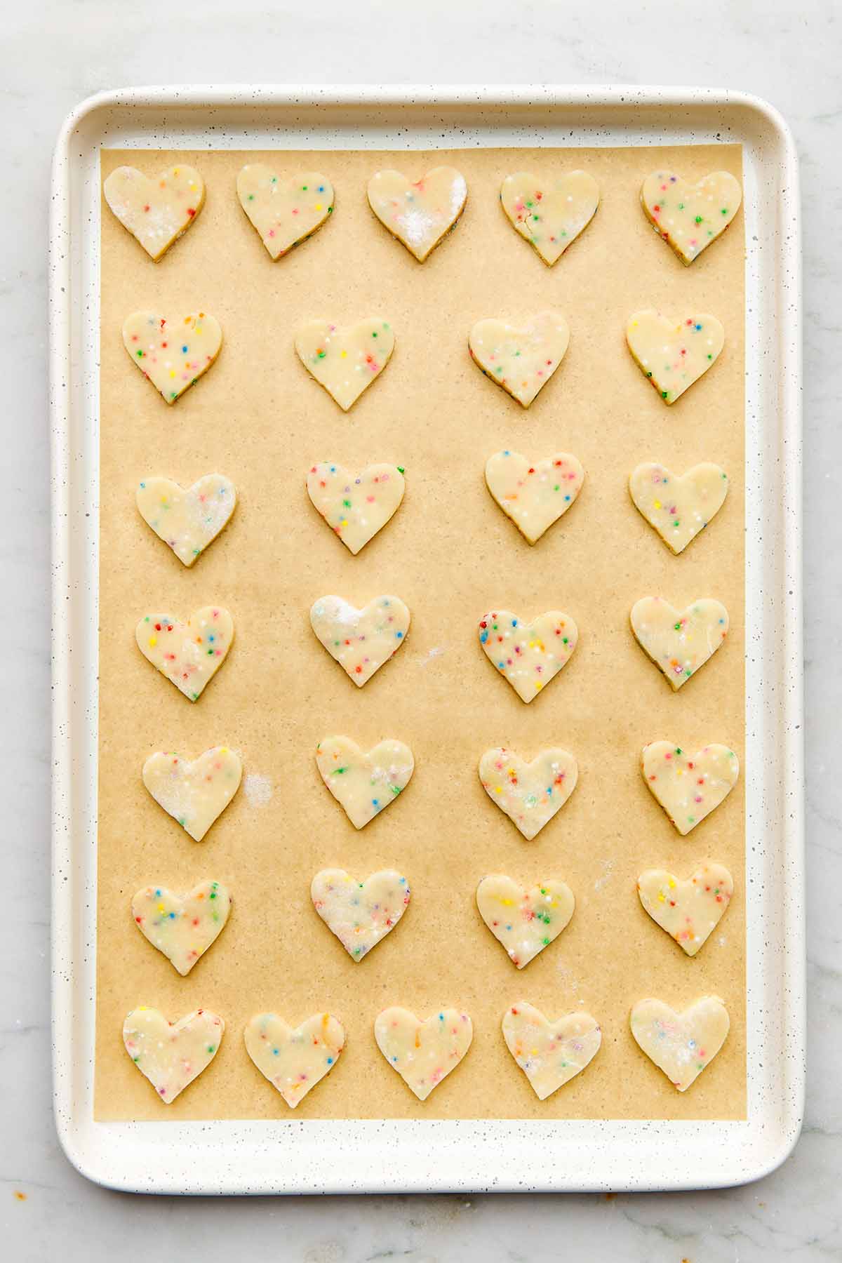 A white baking tray with unbaked cookie cutouts.