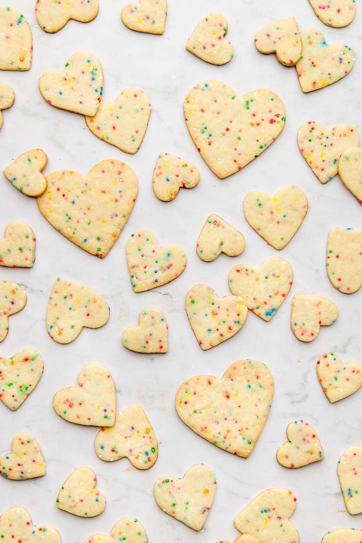 Sugar cookies with sprinkles scattered over a marble surface.