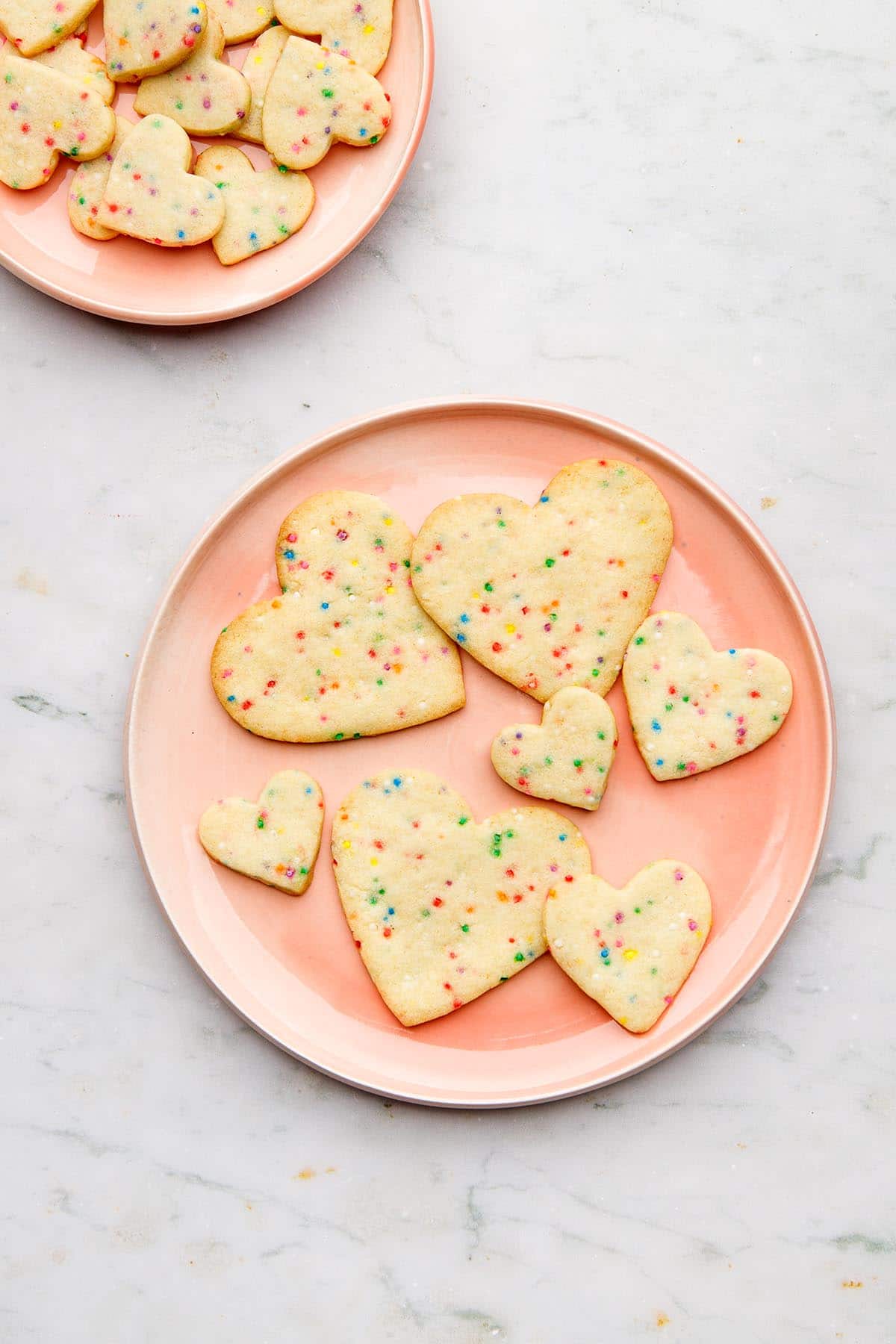 Two pink plates with sugar cookies with sprinkles on them.