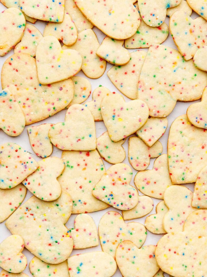 Heart-shaped sugar cookies with sprinkles scattered together over a marble surface.