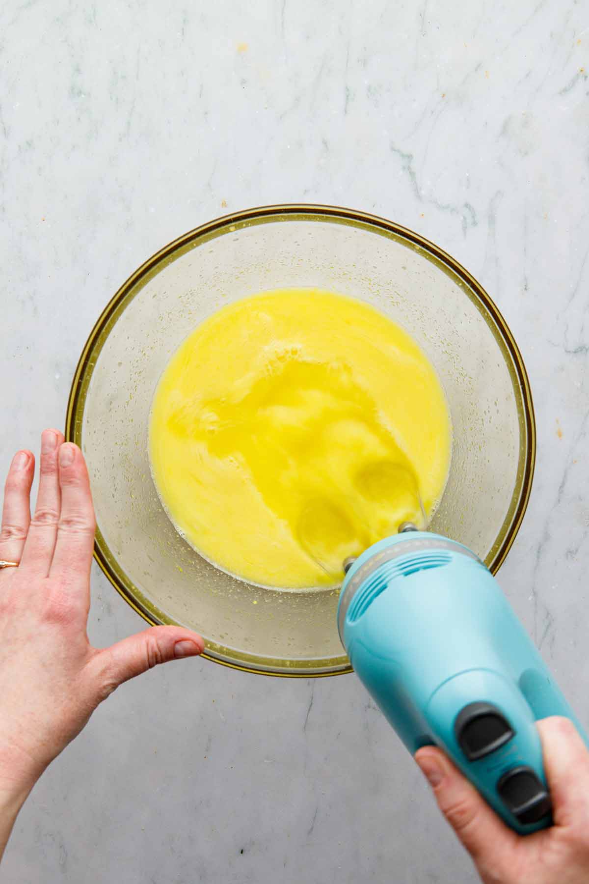 A hand holding a hand mixer and mixing ingredients in a bowl.