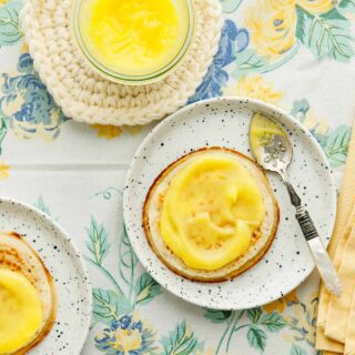 Crumpets on small white plate topped with microwave lemon curd on a blue and yellow flowered tablecloth.
