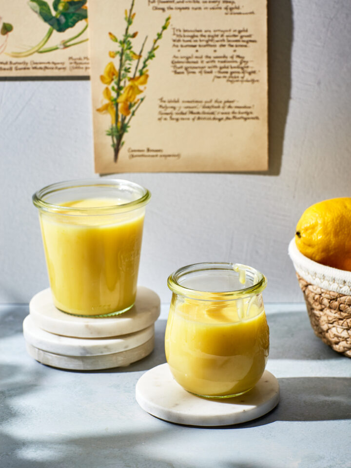 Two jars of microwave lemon curd next to a basket of lemons.