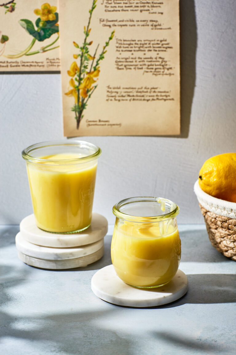 Two jars of microwave lemon curd next to a basket of lemons.