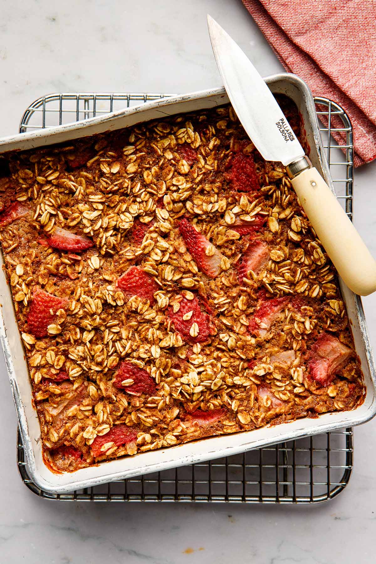 Overhead image of vegan strawberry baked oatmeal in a squre tin with a knife on the edge of the tin.
