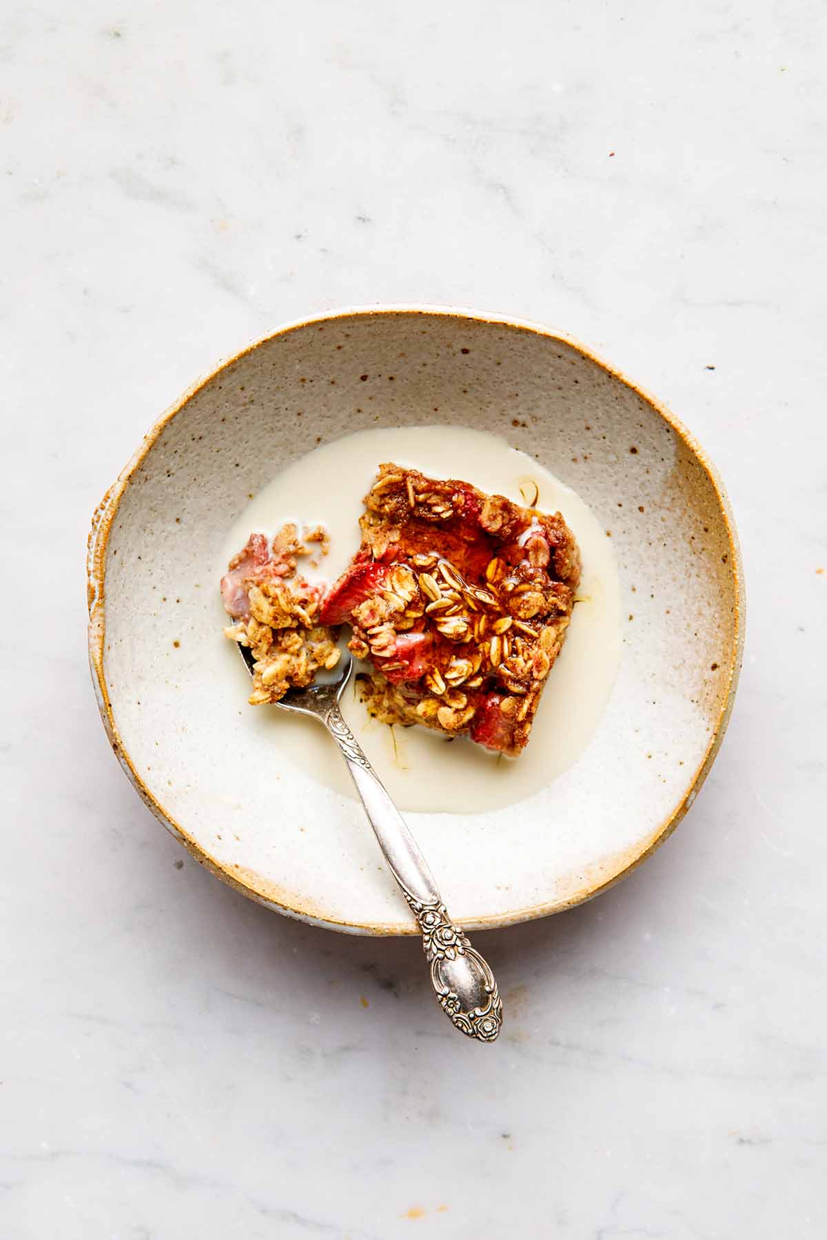 A serving of vegan strawberry baked oatmeal in a ceramic bowl on a marble surface.