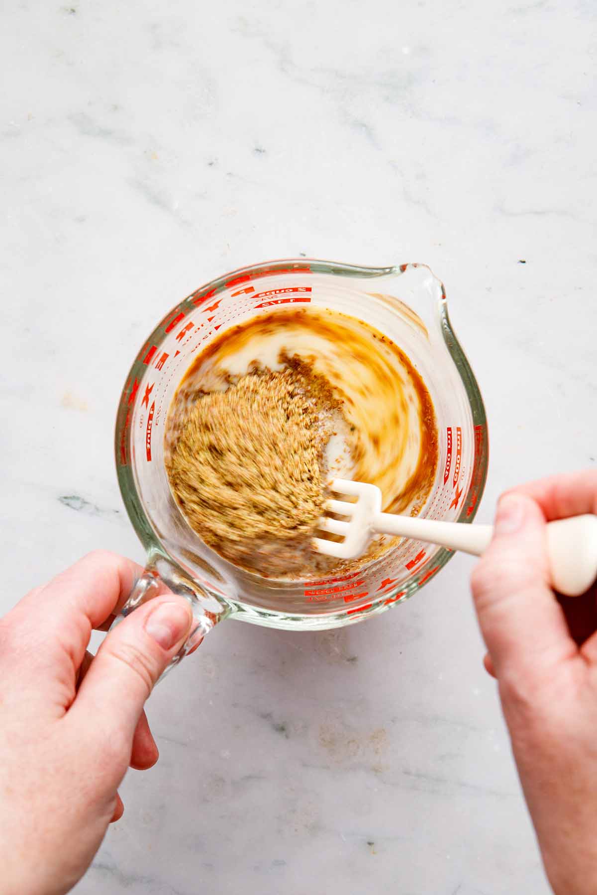A hand using a fork to stir plant-based milk, vanilla, and flax meal in a measuring cup.