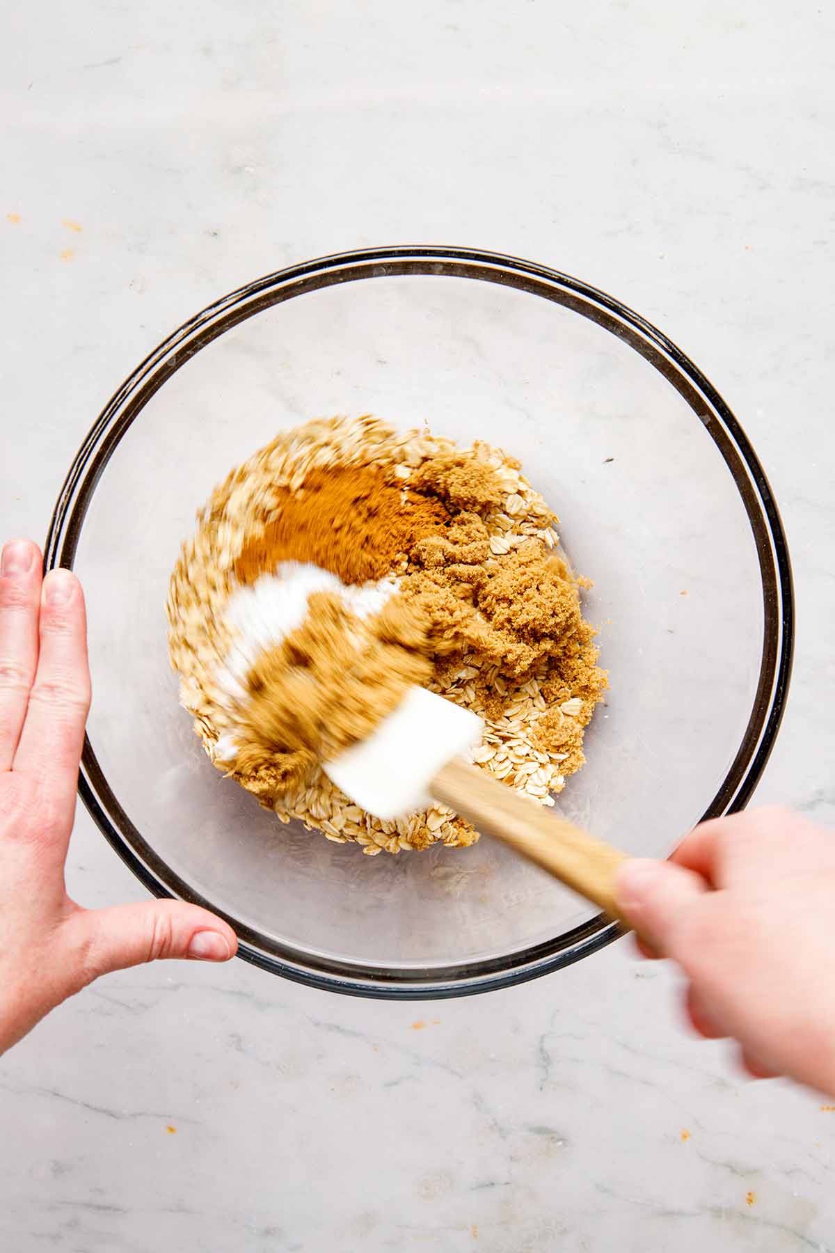 A hand using a rubber spatula to mix dry ingredients in a bowl.