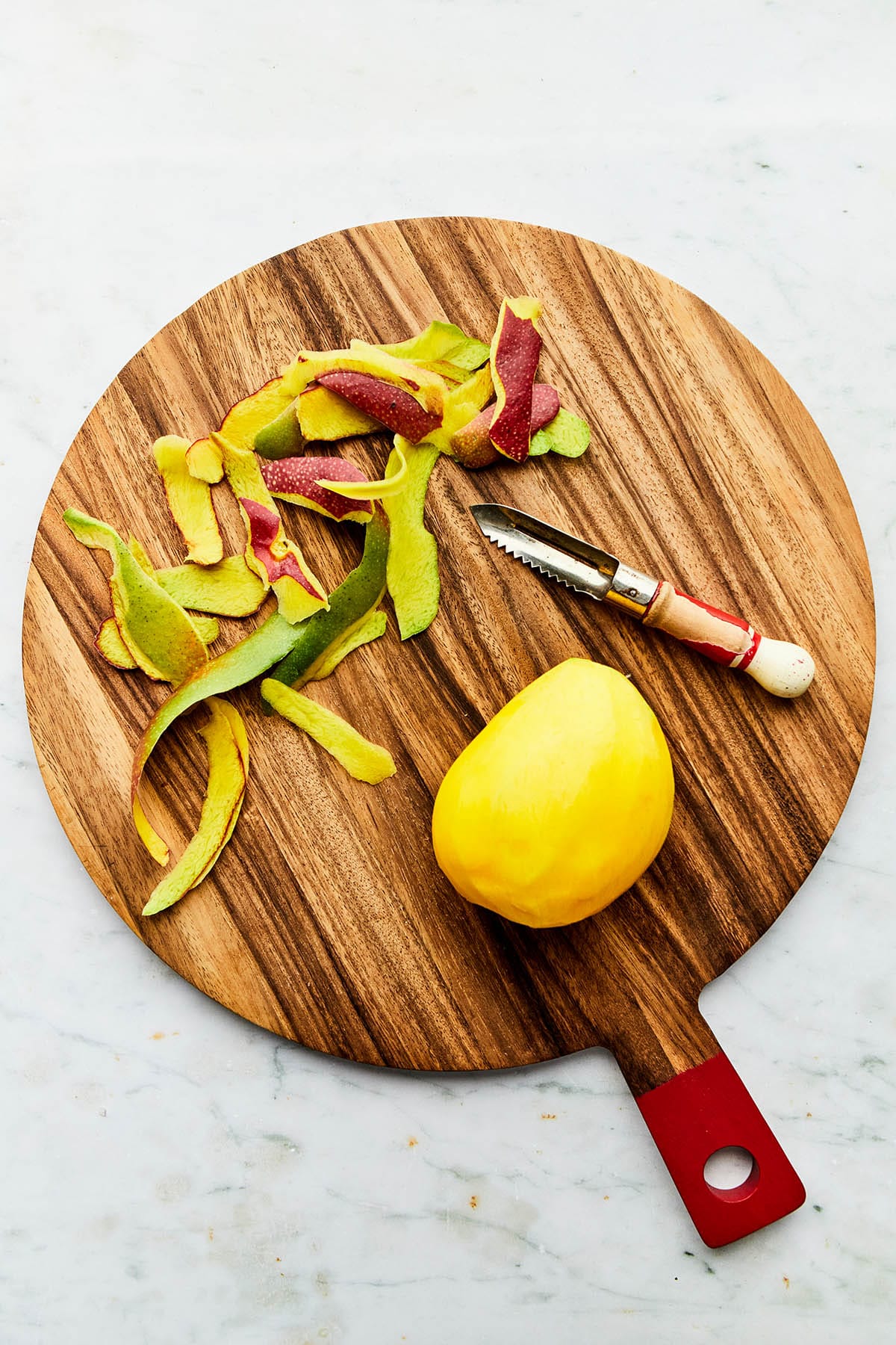 A peeled mango on a cutting board with the peeler alongside.
