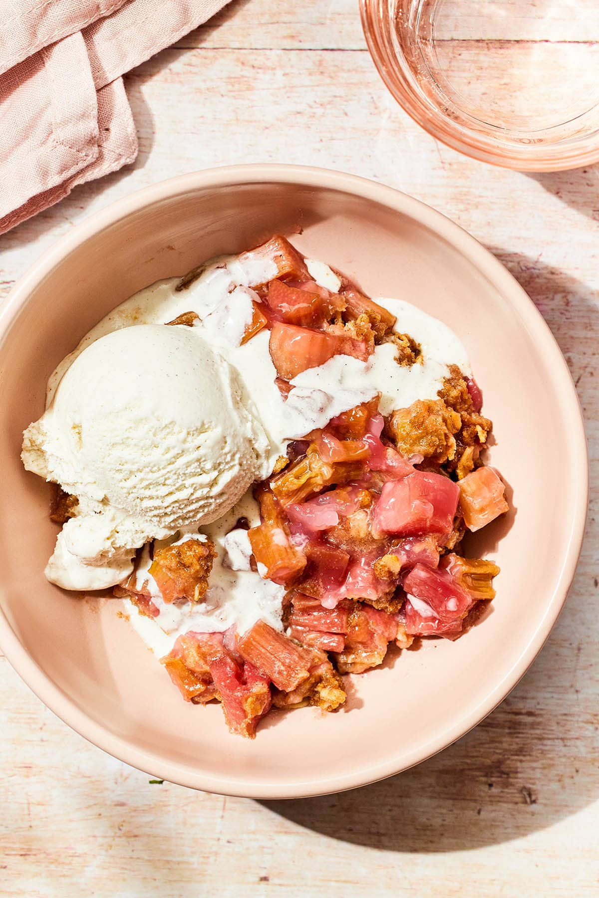 Close up overhead of a pink bowl of gluten-free rhubarb crisp topped with a scoop of ice cream.