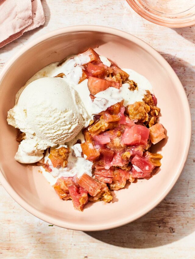 Close up overhead of a pink bowl of gluten-free rhubarb crisp topped with a scoop of ice cream.