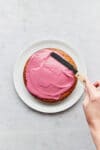 A hand using an offset spatula to spread blackberry glaze on top of a single layer cake.