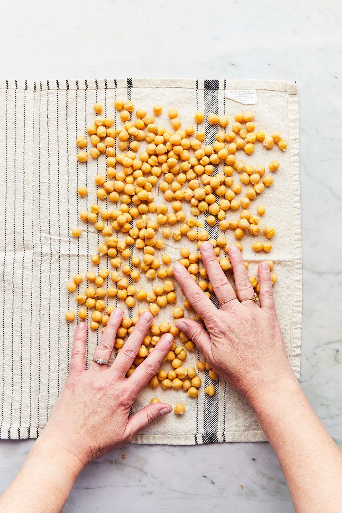 Hands spreading chickpeas evenly over one half of a spread out tea towel.